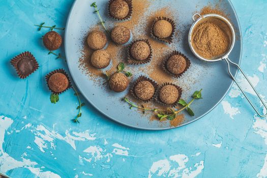 Cocoa balls, handmade chocolate balls cakes in a blue tray, sprinkled with cocoa powder, fresh mint and thyme on dark blue concrete surface background. Close up, copy space, shallow depth of the field