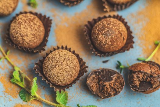 Cocoa balls, handmade chocolate balls cakes in a blue tray, sprinkled with cocoa powder, fresh mint and thyme on dark blue concrete surface background. Close up, copy space, shallow depth of the field