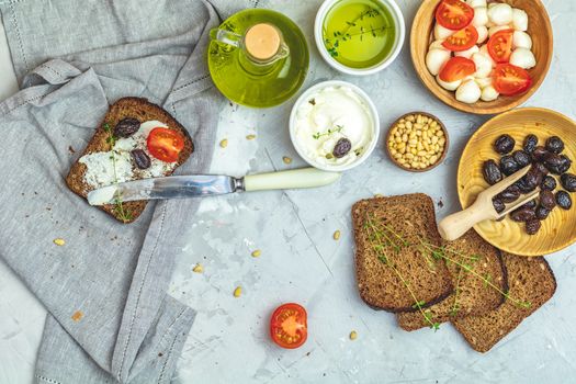 Whole wheat bread baked at home, very healthy with seed, bowl of cream cheese, mozzarella, pine nuts and traditional greek italian appetizer dried olives on light gray concrete table surface.