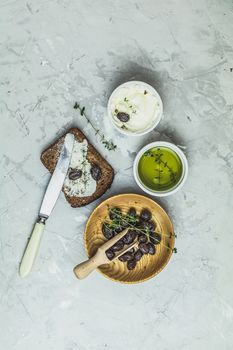Whole wheat bread baked at home, bio ingredients, very healthy with seed, bowl of cream cheese and traditional greek italian appetizer dried olives on light gray concrete table surface.