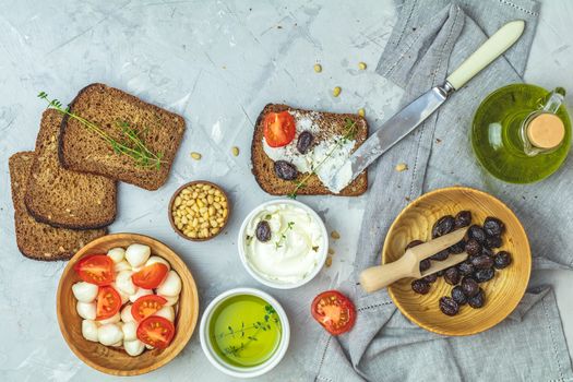 Whole wheat bread baked at home, very healthy with seed, bowl of cream cheese, mozarella, pine nuts and traditional greek italian appetizer dried olives on light gray concrete table surface.