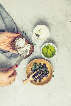 Whole wheat bread baked at home, bio ingredients, very healthy with seed, bowl of cream cheese and traditional greek italian appetizer dried olives on light gray concrete table surface.