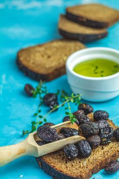 Traditional greek italian appetizer dried black olives with bread and olive oil served on over a blue concrete table surface background