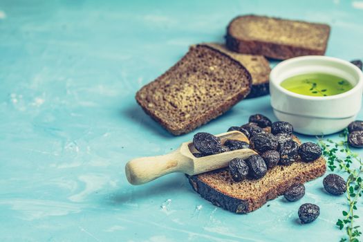 Traditional greek italian appetizer dried black olives with bread and olive oil served on over a blue concrete table surface background