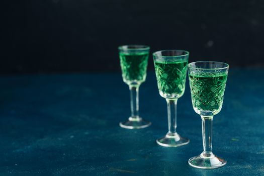 Traditional italian or czech liqueur or bitter with fennel. Three absinthe glass. Dark blue concrete table surface background, copy space for you text.