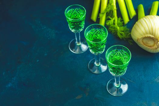 Traditional italian or czech liqueur or bitter with fennel. Three absinthe glass. Dark blue concrete table surface background, copy space for you text.