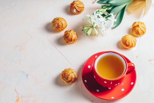 Red in white dotted cup of coffee with milk, delicious profiteroles with cream and white hyacinths on pink concrete surface. Happy Easter, Mothers day, birthday, wedding marriage festive background.