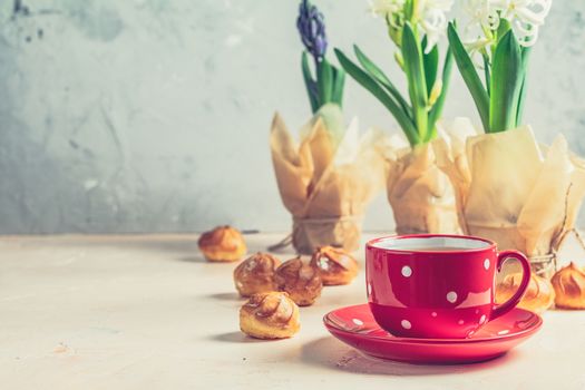 Red in white dotted cup of coffee with milk, delicious profiteroles with cream and white hyacinths on pink concrete surface. Happy Easter, Mothers day, birthday, wedding marriage festive background.