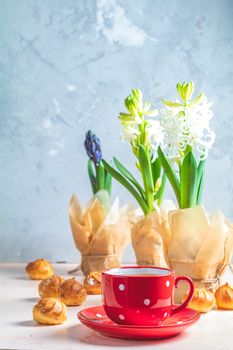 Red in white dotted cup of coffee with milk, delicious profiteroles with cream and white hyacinths on pink concrete surface. Happy Easter, Mothers day, birthday, wedding marriage festive background.