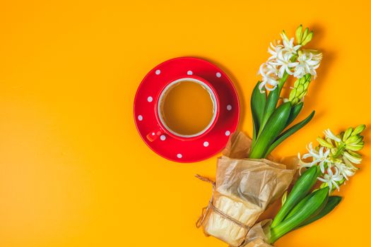 Red in white dotted cup of tea beside white hyacinths on yellow surface background. Minimalism, top view, copy space for you text.