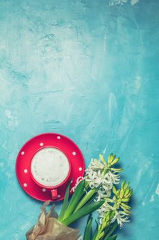 Red in white dotted cup of coffee with milk and white hyacinths on blue concrete surface background. Top view, copy space. Beautiful spring greeting card.