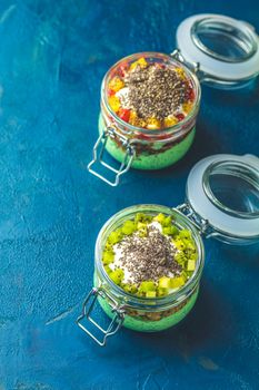 Two chia seed pudding with matcha green tea, kiwi and granola, orange in glasses on dark blue concrete background. Healthy breakfast.