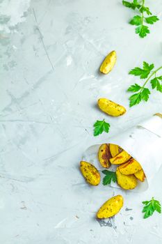 Baked potato wedges on paper with addition sea salt and parsley on a light gray concrete background