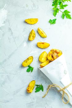 Baked potato wedges on paper with addition sea salt and parsley on a light gray concrete background