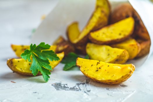 Baked potato wedges on paper with addition sea salt and parsley on a light gray concrete background