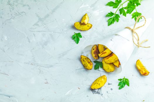 Baked potato wedges on paper with addition sea salt and parsley on a light gray concrete background