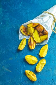 Baked potato wedges on paper with addition sea salt on a dark blue concrete background