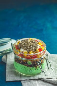 Chia seed pudding with matcha green tea, orange and granola in glass on dark blue concrete background. Healthy breakfast.