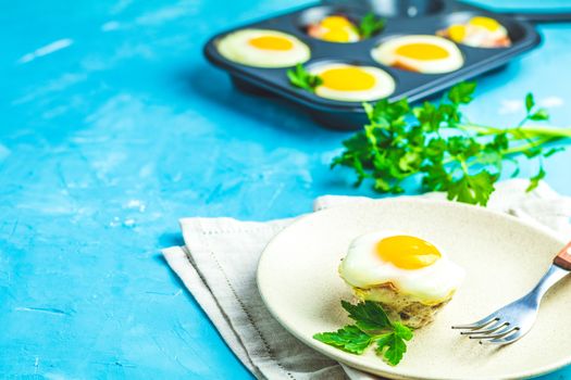 Baked eggs  in light plate and baking molds. Portioned casserole from bacon  and eggs in Italian style. Blue concrete table surface background.