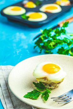 Baked eggs  in light plate and baking molds. Portioned casserole from bacon  and eggs in Italian style. Blue concrete table surface background.