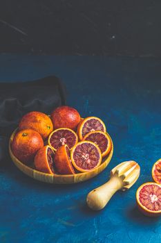 Sicilian half blood oranges squeezed and cut squeezed in wooden plate over dark blue concrete table surface. Dark rustic style.