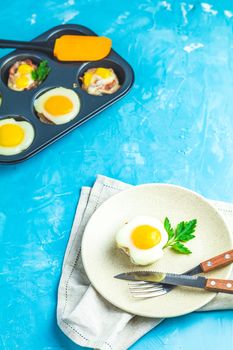 Baked eggs  in light plate and baking molds. Portioned casserole from bacon  and eggs in Italian style. Blue concrete table surface background.