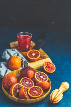 Shorts of alcohol cocktail with Sliced Sicilian Blood oranges and fresh red orange juice, served on dark blue concrete table surface. Dark rustic style.