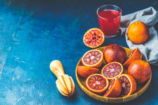 Shorts of alcohol cocktail with Sliced Sicilian Blood oranges and fresh red orange juice, served on dark blue concrete table surface. Dark rustic style.