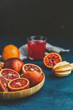 Shorts of alcohol cocktail with Sliced Sicilian Blood oranges and fresh red orange juice, served on dark blue concrete table surface. Dark rustic style.