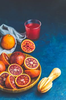 Shorts of alcohol cocktail with Sliced Sicilian Blood oranges and fresh red orange juice, served on dark blue concrete table surface. Dark rustic style.