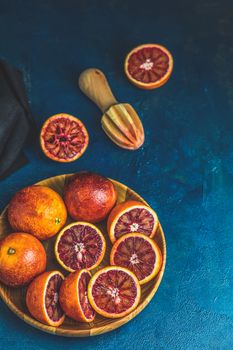 Sicilian half blood oranges squeezed and cut squeezed in wooden plate over dark blue concrete table surface. Dark rustic style.