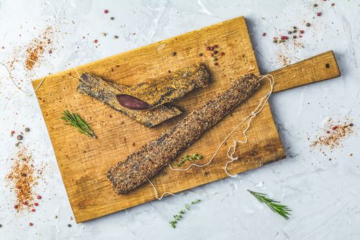 Jerky, basturma, dried meat beef, meat smoked jerky with spices on wooden cutting board, top view, light gray concrete surface table background.