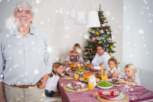 Composite image of Smiling grandfather standing at the dinner table against snow falling