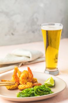 Fried Shrimps tempura with lime in light plate and glass of beer on pink or peach concrete surface background. Copy space Seafood tempura dish served japanese or eastern Asia style with chopsticks