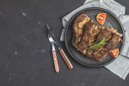 Delicious baked roast pork meat in black ceramic plate with garlic and spices. Dish for dinner. Top view, flat lay, dark concrete surface, copy space for you text