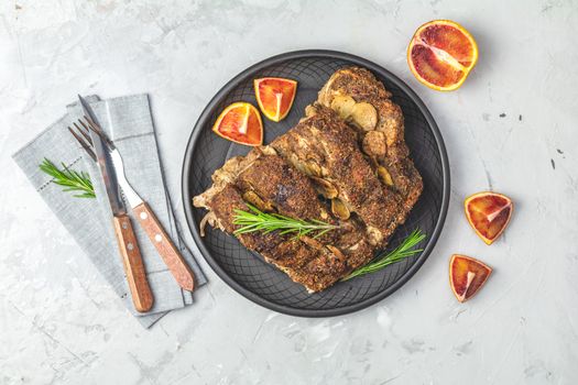 Delicious baked roast pork meat in black ceramic plate with garlic and spices. Dish for dinner. Top view, flat lay, gray concrete surface, copy space for you text