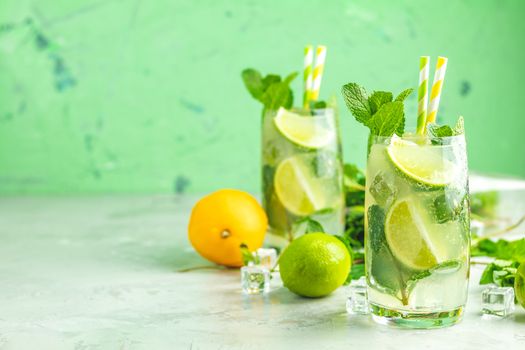 Two mojito cocktails with lime and mint in highball glasses on a gray and green concrete stone surface background. With copy space for your text
