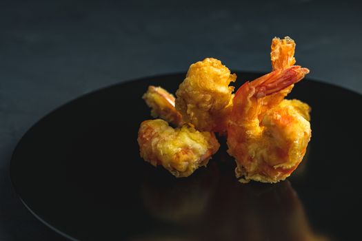 Fried Shrimps tempura in black plate on dark concrete surface background. Copy space for you text. Seafood tempura dish served japanese or eastern Asia style with chopsticks.