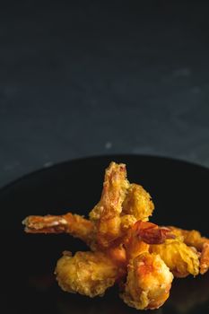 Fried Shrimps tempura in black plate on dark concrete surface background. Copy space for you text. Seafood tempura dish served japanese or eastern Asia style with chopsticks.