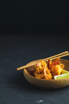 Fried Shrimps tempura with lime in wooden plate on dark concrete surface background. Copy space for you text. Seafood tempura dish served japanese or eastern Asia style with chopsticks.