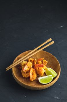 Fried Shrimps tempura with lime in wooden plate on dark concrete surface background. Copy space for you text. Seafood tempura dish served japanese or eastern Asia style with chopsticks.