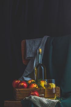 Apple cider vinegar or fruits tea with apple slices in glass with ripe red apples in box, dark vintage rustic style. Shallow depth of the field.