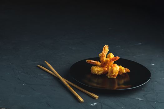 Fried Shrimps tempura in black plate on dark concrete surface background. Copy space for you text. Seafood tempura dish of traditional asian cuisine.