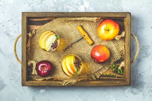 Glasses of homemade organic apple cider with fresh apples in box, top view, light gay concrete table surface.