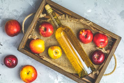 Bottle of homemade organic apple cider with fresh apples in box, top view, light gay concrete table surface.