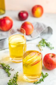 Bottle and glasses of homemade organic apple cider with fresh apples in box, light concrete table surface. Shallow depth of the field.