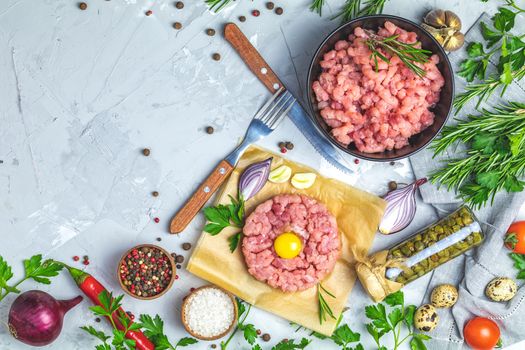 Healthy food, cooking concept. Homemade raw organic minced beef meat and steak tartare with yolk with vegetables on light gray stone concrete textured surface background. Copy space background, top view flat lay.