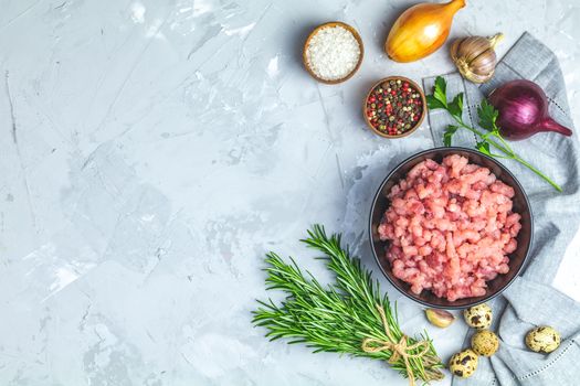 Homemade minced meat in a black bowl over light gray slate or stone or concrete background with ingredients for making. Top view with copy space.