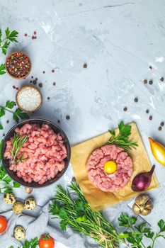 Healthy food, cooking concept. Homemade raw organic minced beef meat and steak tartare with yolk with vegetables on light gray stone concrete textured surface background. Copy space background, top view flat lay.