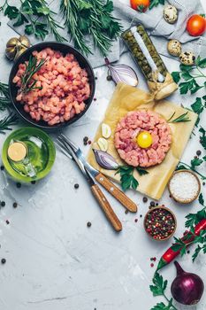 Healthy food, cooking concept. Homemade raw organic minced beef meat and steak tartare with yolk with vegetables on light gray stone concrete textured surface background. Copy space background, top view flat lay.